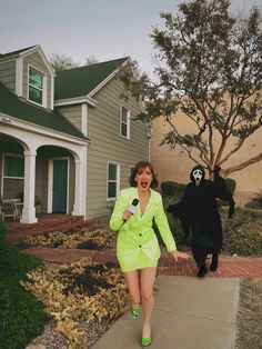 a woman in a neon green suit walking down a sidewalk next to a black cat