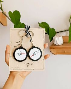 a pair of black and white keychains with hand prints on them, held in front of a plant