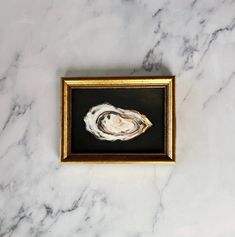 an abstract painting on a marble surface with gold frame and black background, in the shape of a seashell