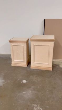 two wooden boxes sitting next to each other in a room with white walls and cement flooring