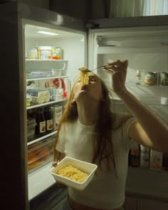 a woman eating food out of a white container in front of an open refrigerator door