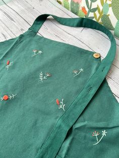 a green apron with embroidered flowers on it sitting on a table next to a pillow