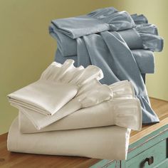 a stack of folded sheets on top of a wooden table next to a blue dresser