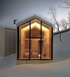 a small wooden cabin in the snow with its windows open and lit up at night