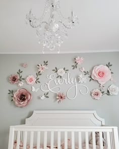 a white crib with pink flowers on the wall and chandelier above it