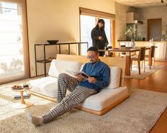 a man sitting on top of a white couch in a living room next to a table