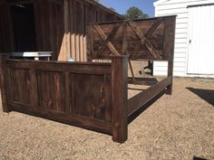 a wooden bed frame sitting in the middle of a dirt field next to a barn