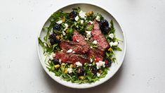 a white bowl filled with meat and salad on top of a table next to a fork