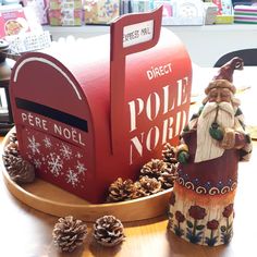 a mailbox with a santa claus figure next to it and pine cones on the table