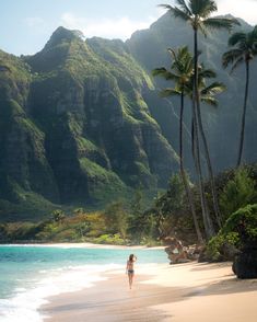 a woman standing on the beach in front of mountains and palm trees with her back to the camera