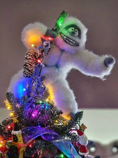 a white stuffed animal is sitting on top of a christmas tree with lights and decorations