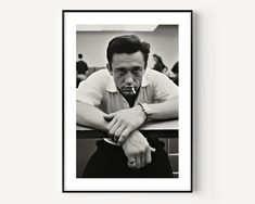 a black and white photo of a man sitting at a table with his hand on his chin