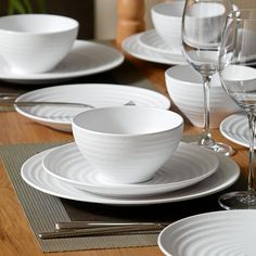 the table is set with white dishes and silver cutlery, wine glasses, and placemats