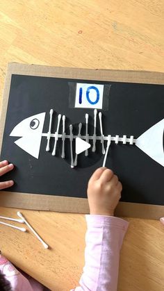 a child is making a fish skeleton out of construction paper and stringing it on the table