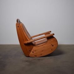 a wooden rocking chair sitting on top of a cement floor next to a white wall