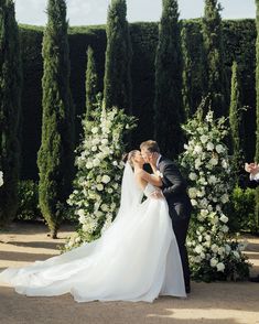 a bride and groom kissing in front of an outdoor wedding ceremony arch with white flowers