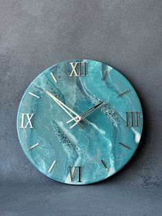 a blue clock with roman numerals is on a gray surface and it's hands are in the air