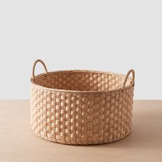 a woven basket with handles sits on a table, ready to be used as a storage container