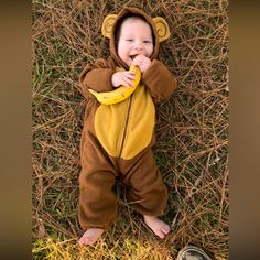 a baby wearing a monkey costume laying on the ground with a banana in his mouth