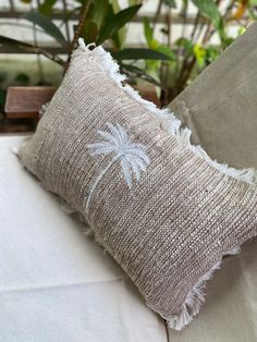 a pillow that has been placed on top of a couch with some plants in the background