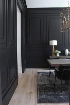 a dining room with black walls and wood flooring is pictured in this image, there are two lamps on the table