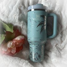 a blue travel mug sitting on top of a white blanket next to a pink flower