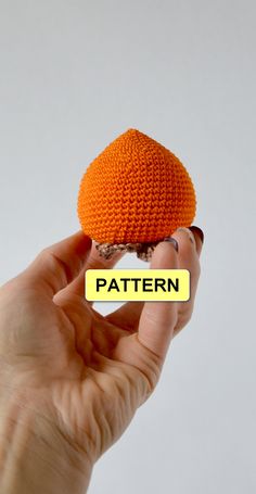 a hand holding an orange crocheted object with the word pattern on it