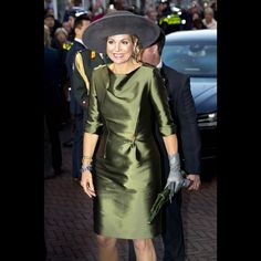 a woman in a green dress and hat walking down the street with other people behind her