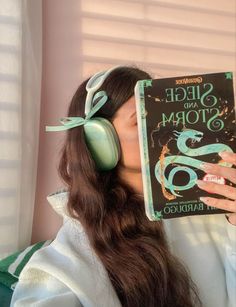 a woman wearing headphones and holding up a book in front of her face to the side