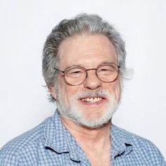 an older man with glasses and a beard smiling at the camera while standing in front of a white background