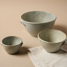 three white bowls sitting next to each other on top of a brown tablecloth and napkin