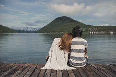 two people sitting on a dock looking out at the water