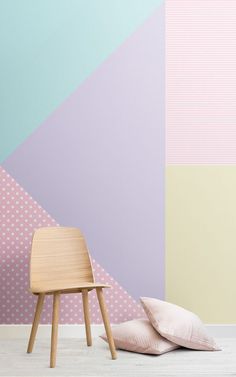 a wooden chair sitting next to a pink pillow on top of a white floor in front of a colorful wall