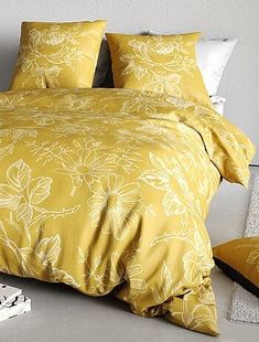 a bed with yellow comforter and pillows on top of it next to a nightstand