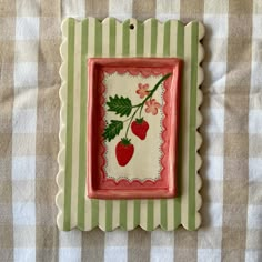 a small red and green plate with strawberries on it's edge, sitting on a checkered tablecloth