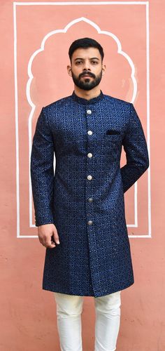 This blue Sherwani has a distinctive mandarin collar and a row of hand polished dark silver buttons down the front. It features long sleeves and has a same colour woven pattern on it. The matching churidar pants are also made with the same golden woven design. The included dupatta is made of golden net or your choice and has a similar design to complete the look. The Sherwani is made of imported fabric and is available in blue as well as other colour if available on your demand. The package includes this beautiful Sherwani, Churidar pants This elegant Sherwani suit is ideal for formal events, parties and evening dinners. Customization options are available for size, design and colour to suit your personal style and taste. We can also give you a turban, jooti, mojari of your matching outfit Men’s Bandhgala, Dark Blue Sherwani, Men Sherwani Designs Style, Shervani Design For Men Simple, Indowestern Outfits For Men Indian Weddings, Indian Wedding Outfit Men, Mens Kurta Designs Wedding, Blue Sherwani Groom, Jotpuri Suit For Men