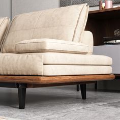 a beige couch sitting on top of a wooden floor next to a book shelf and lamp