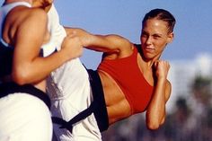 two women practicing martial on the beach with one woman in red top and white pants