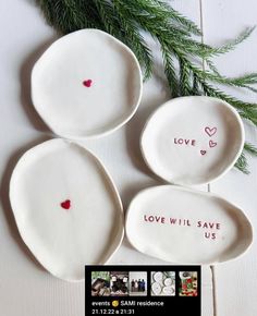 three white plates with red hearts and love will save us written on the side, sitting next to some evergreen branches