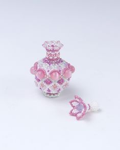 a small pink and white beaded perfume bottle next to a tiny pearled butterfly