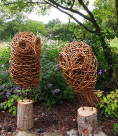 two sculptures made out of branches in the middle of a garden with flowers and trees