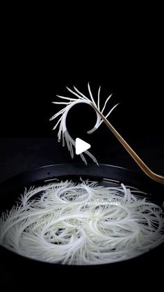 white noodles being cooked in a pan with a wooden spoon on the side and black background