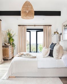 a bedroom with white bedding and beige drapes on the sliding glass doors that lead to an outside patio