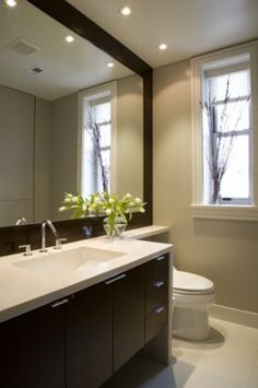 a white toilet sitting next to a bathroom sink under a window in front of a mirror