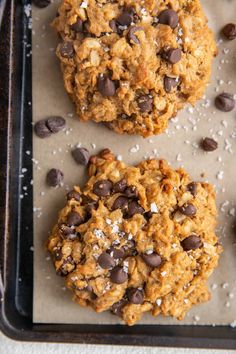 two oatmeal cookies on a baking sheet with chocolate chips and coconut flakes