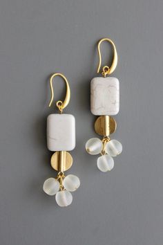 two pairs of white and gold earrings on a gray surface with one pair hanging off the side