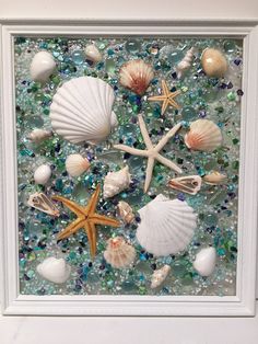 sea shells and starfish are arranged in a white frame on the beach glass mosaic