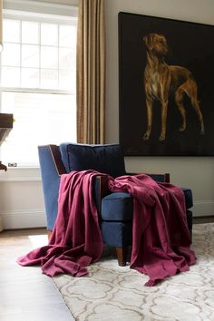 a living room with a blue chair and a painting on the wall