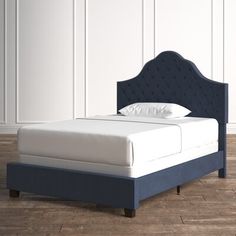 a bed with a blue headboard and white sheets on it, against a white wall