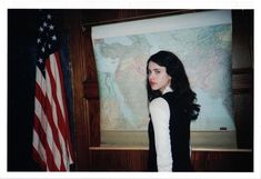 a woman standing next to an american flag in front of a map and wooden paneled wall